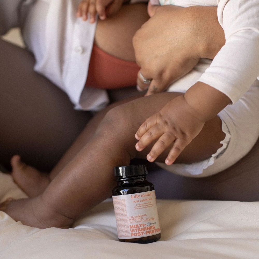 Une femme allaite un bébé. Une bouteille avec l'étiquette: JOLLY MAMA Post Essentials, Multi-Vitamine Post-Partum.