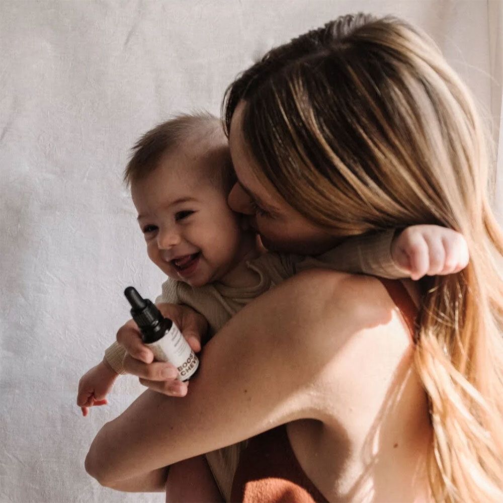 Femme tenant un bébé dans ses bras. Le bébé sourit. La femme tient une bouteille avec un compte-gouttes.