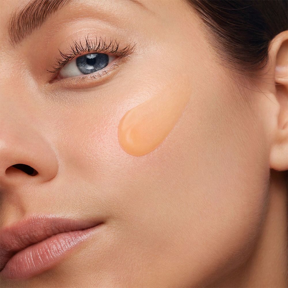 Gros plan d'un visage avec un échantillon de gel orangé appliqué sur la joue. Teint clair.