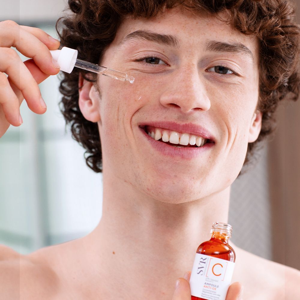 Un homme tient un flacon avec compte-gouttes. Gouttes sur le visage. Étiquette: SVR [C] Ampoule Anti-Ox.