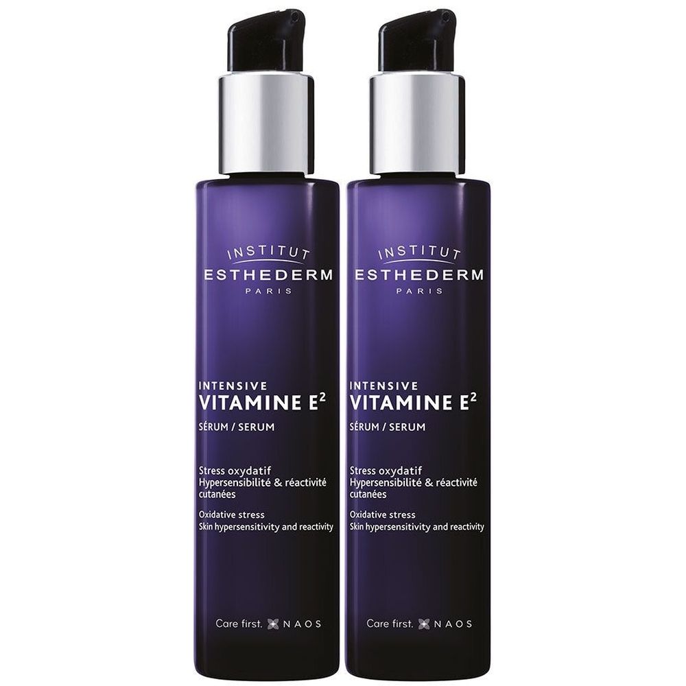 Deux flacons de sérum violets avec pompes argentées. Inscription: INSTITUT ESTHEDERM, INTENSIVE VITAMINE E2. Texte en anglais et français.