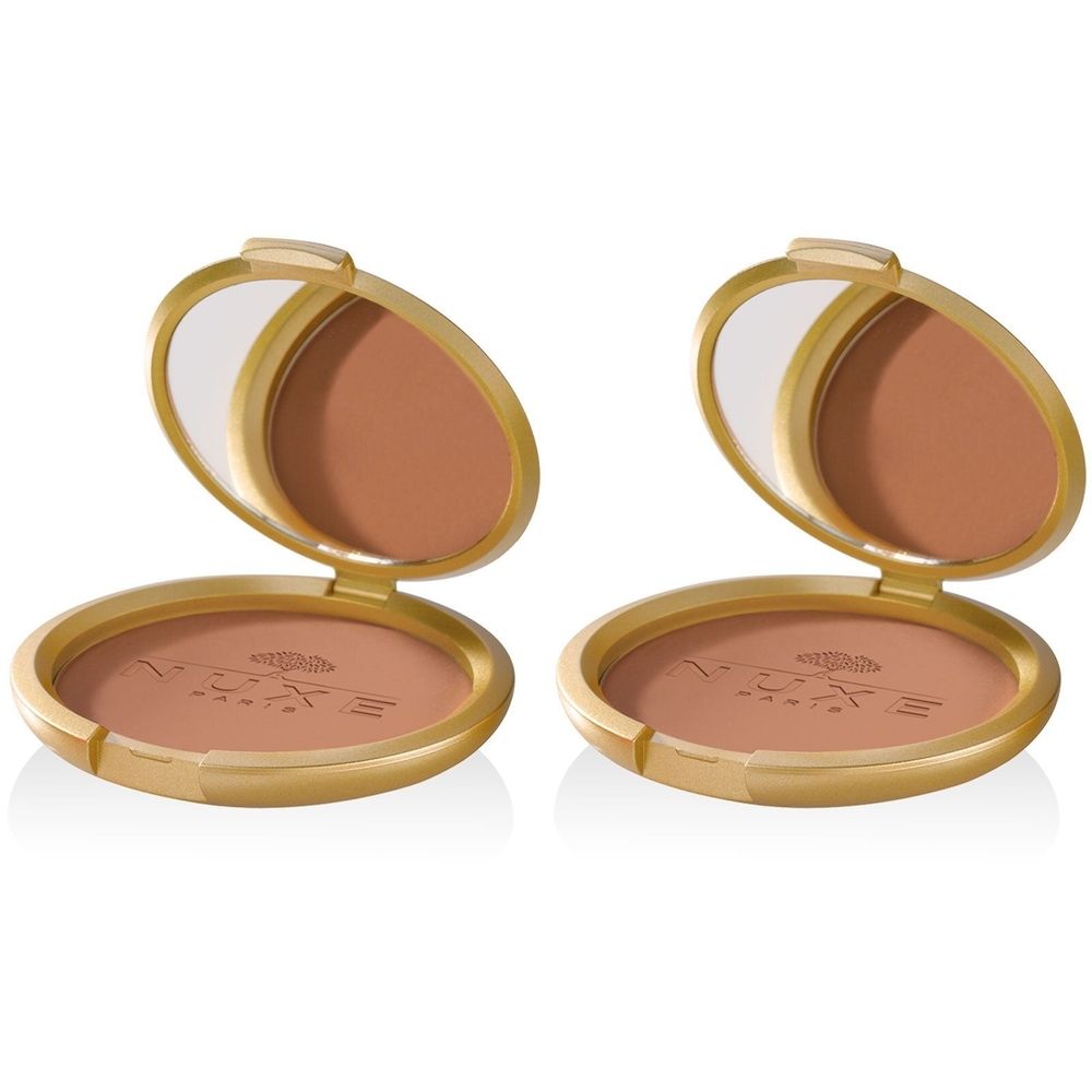 Deux poudriers dorés ouverts, avec miroir et poudre bronzante. Le nom de la marque Nuxe est visible sur la poudre.