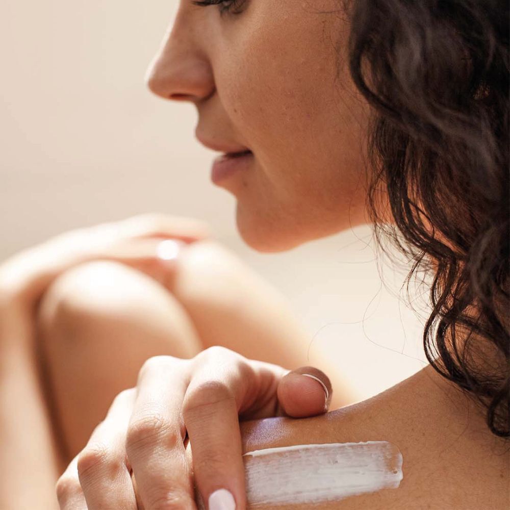 Gros plan d'une personne appliquant de la crème sur l'épaule. Bande de crème visible. Arrière-plan flou.