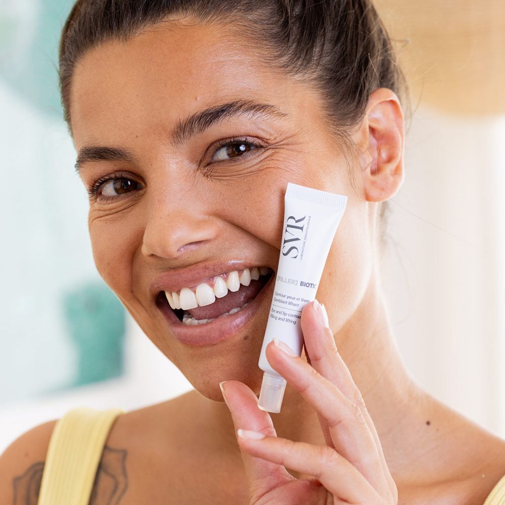 Femme tenant un tube de SVR [Filler] Biotic. Nom du produit visible. La femme sourit.