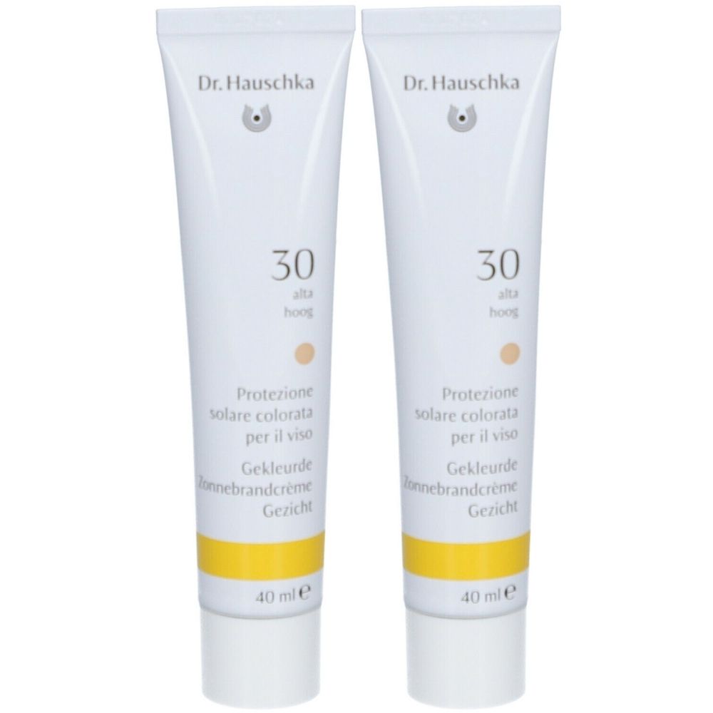 Deux tubes de crème solaire teintée Dr. Hauschka SPF 30. Tubes blancs avec bande jaune et indications multilingues.