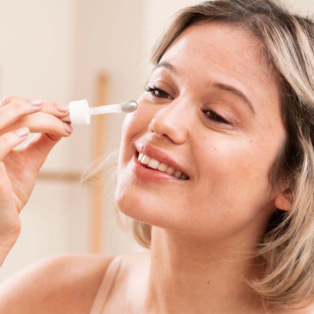 Femme tenant une pipette devant l'œil. Aucun produit visible.