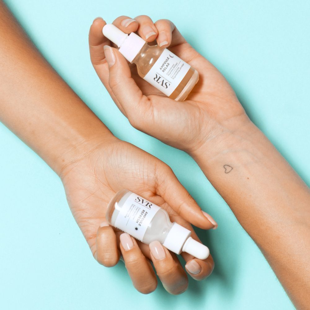 Deux flacons dans les mains. Inscription : SVR, Ampoule Refresh, Eye concentrate. Une main a un tatouage.