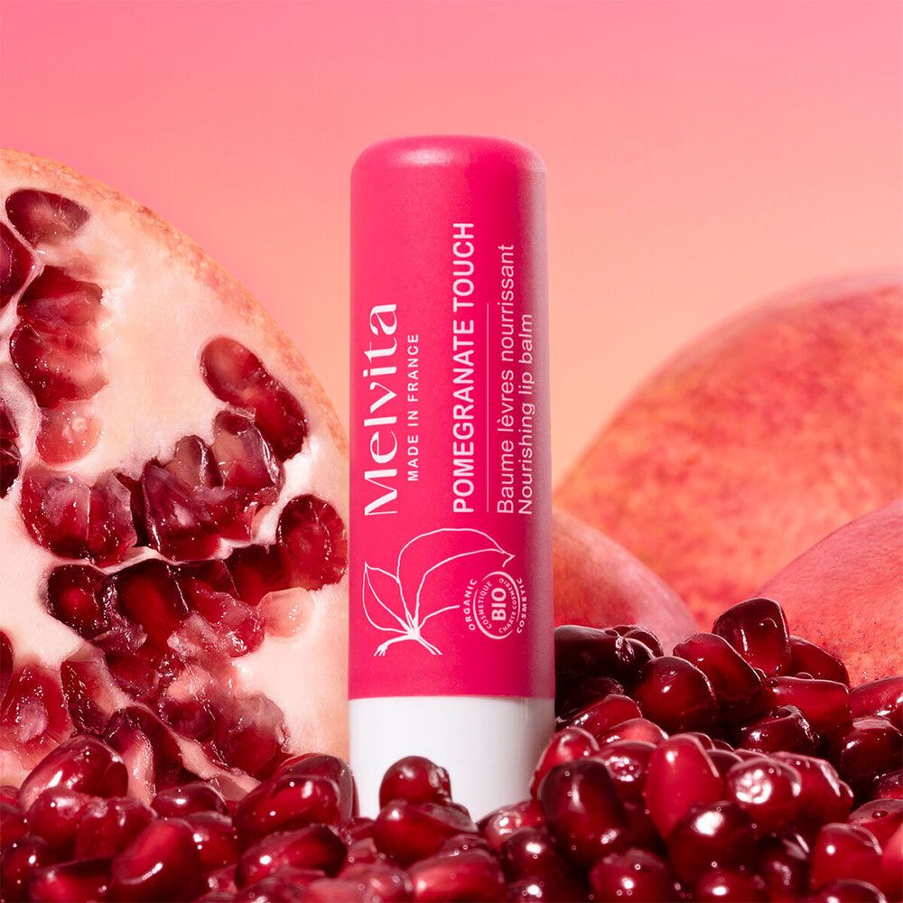 Stick de baume à lèvres rose avec logo Melvita, motif grenade et label bio. Entouré de fruits et de graines de grenade.