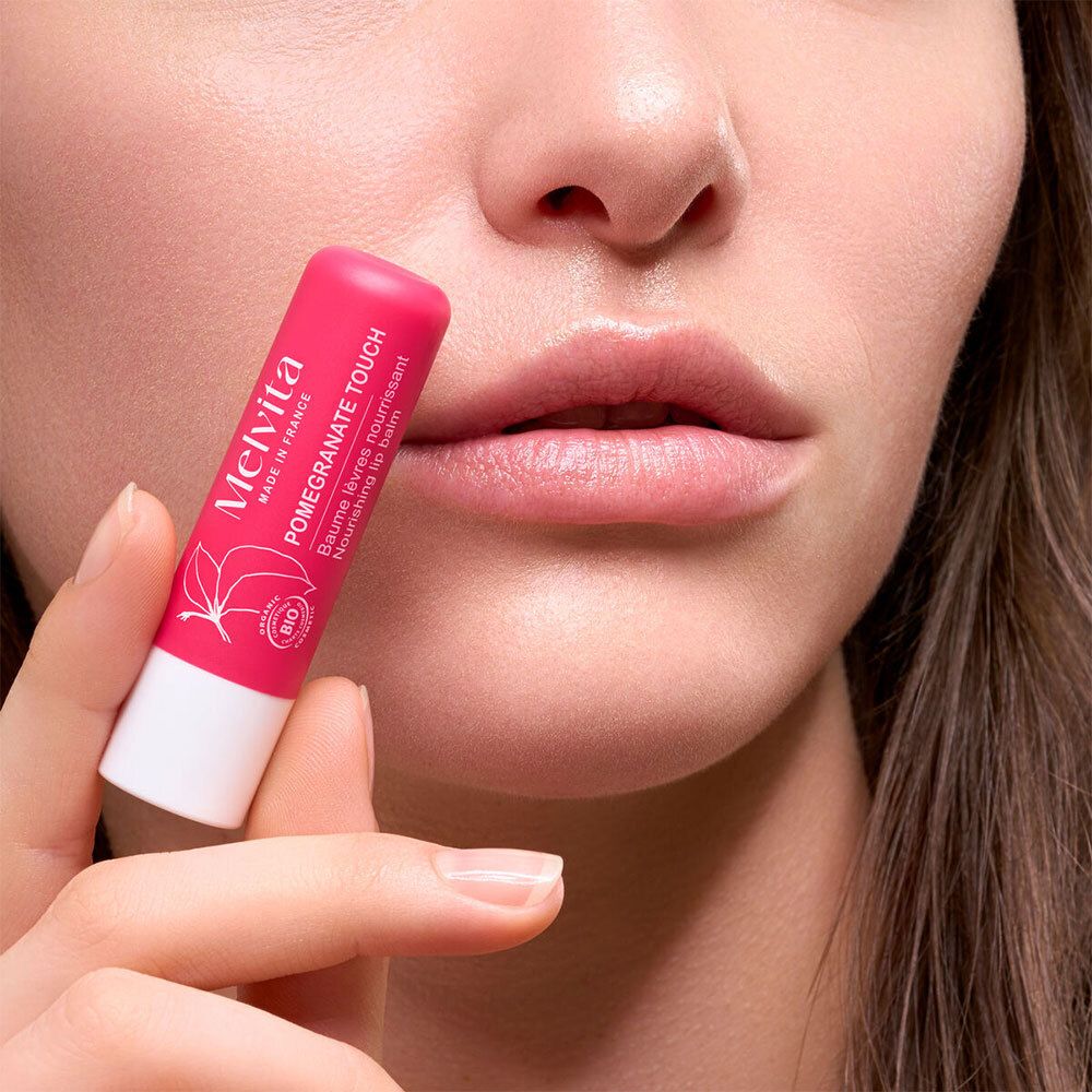 Personne tenant un stick de baume à lèvres rose devant ses lèvres. Sur le stick : Pomegranate Touch, Melvita, label bio.