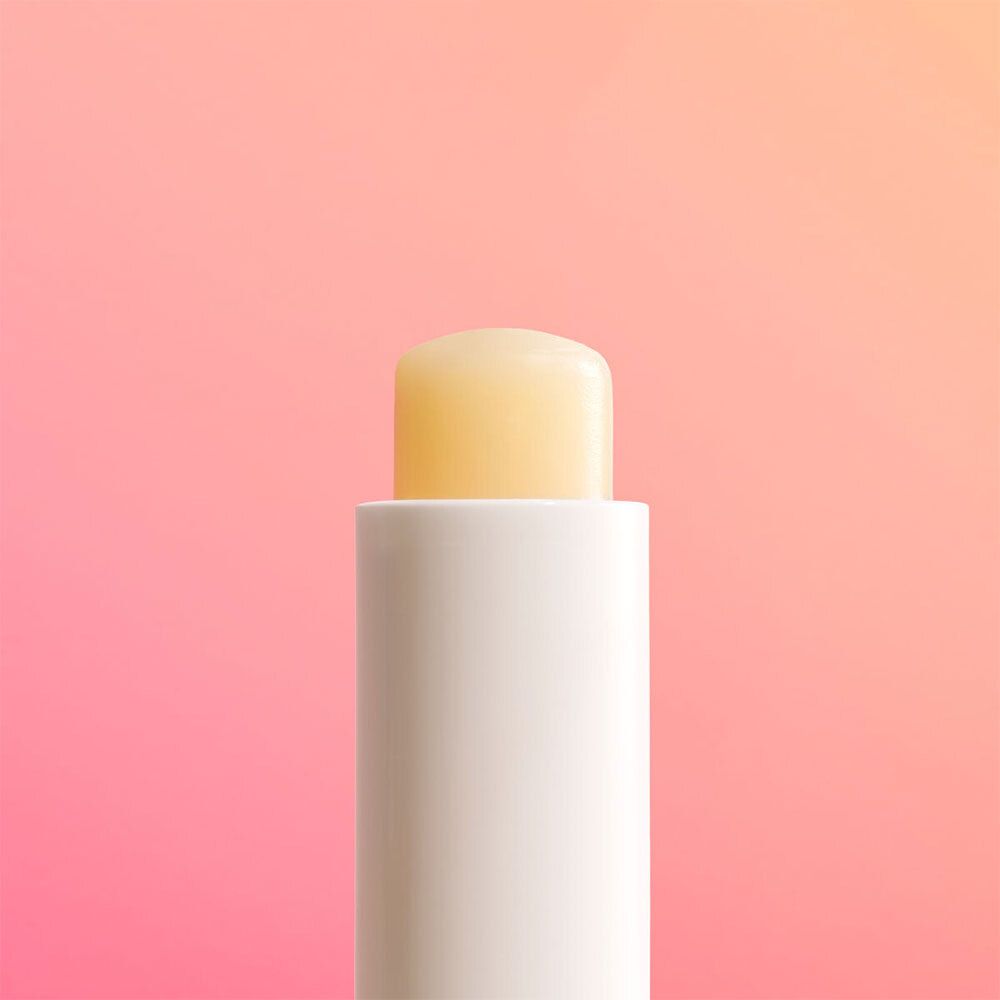 Gros plan d'un stick de baume à lèvres blanc avec baume jaune. Le stick est placé sur un fond rose.