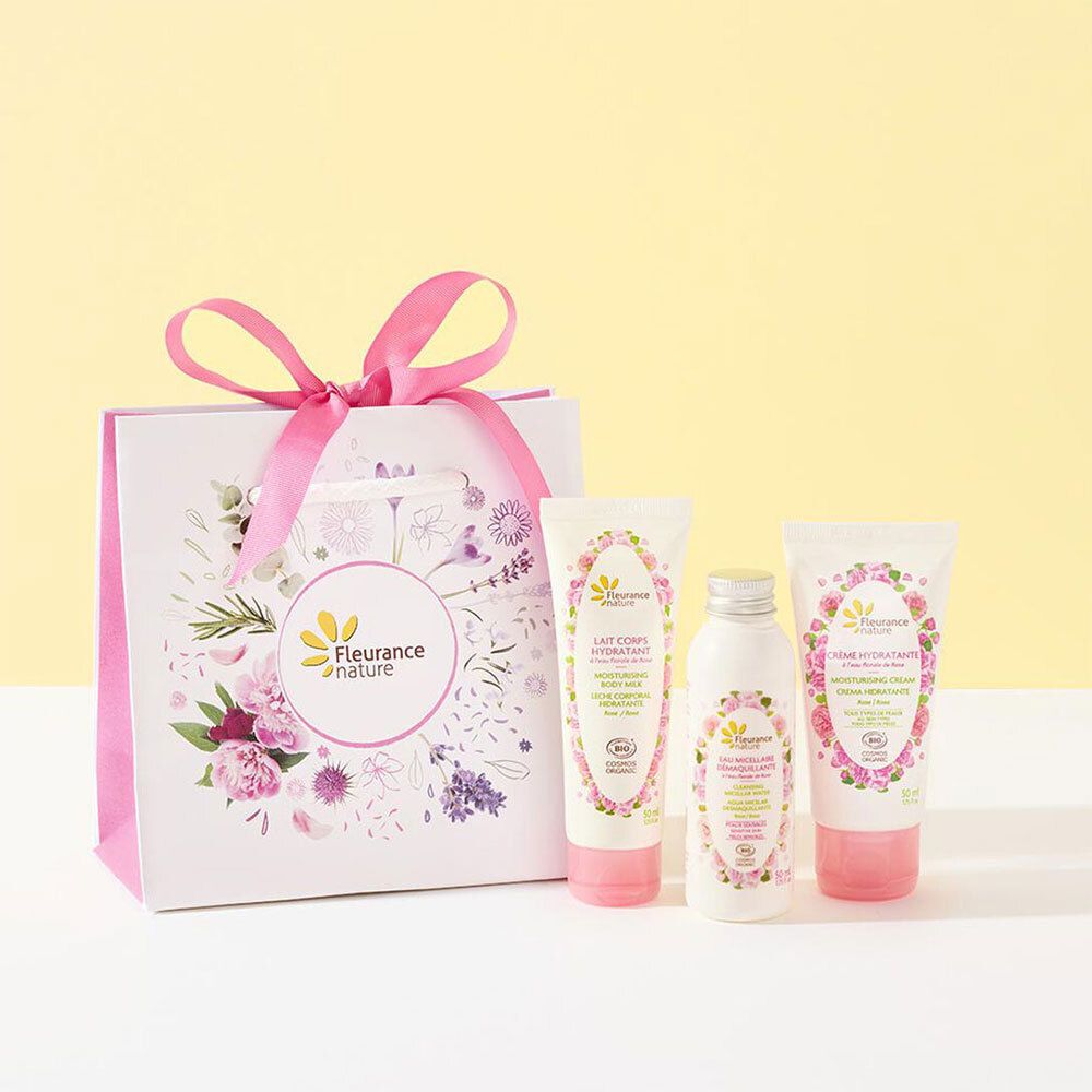 Sac cadeau avec trois produits cosmétiques. Le sac est blanc avec des accents roses et des motifs floraux. Produits avec tubes roses et blancs.