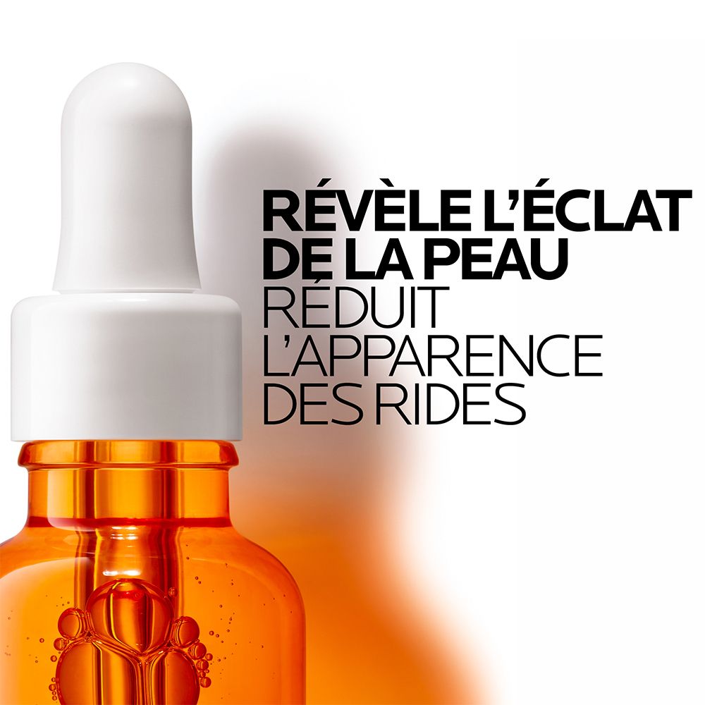 Gros plan d'un flacon de sérum. Texte : Révèle l'éclat de la peau, réduit l'apparence des rides. Sérum orange.