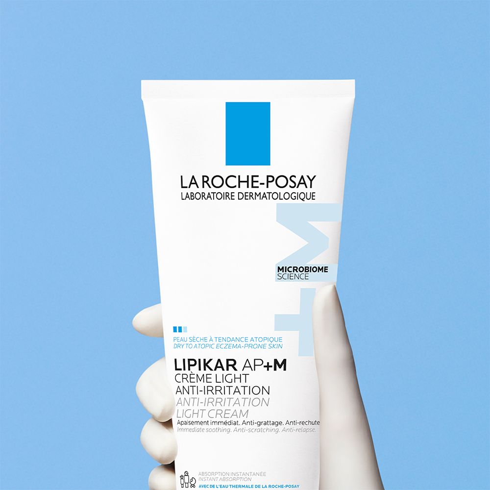 Tube blanc dans une main. Texte: LA ROCHE-POSAY, LIPIKAR AP+M Crème Light Anti-Irritation. Fond bleu.