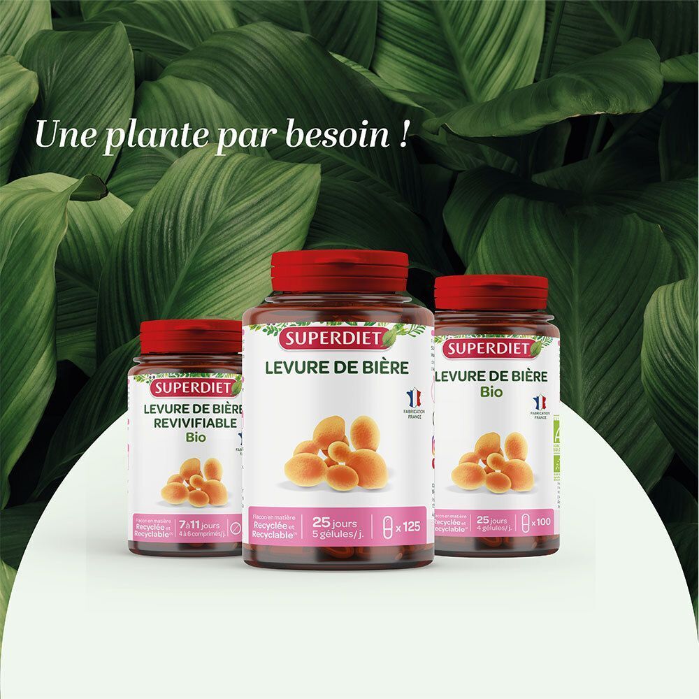 Trois flacons de Superdiet Levure de Bière Bio de différentes tailles, sur une table devant un motif de feuilles vertes.