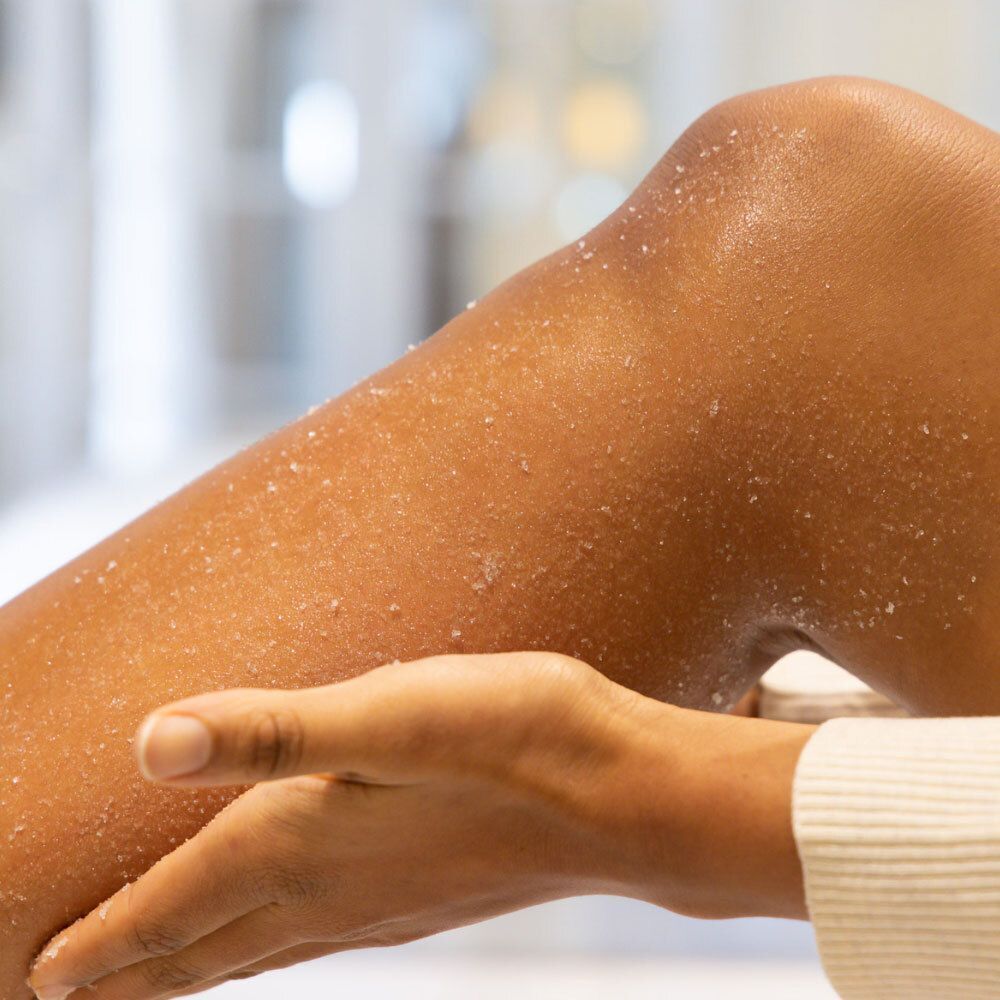 Jambe avec gommage au sel. Main touchant la jambe. Produit de soin de la peau.