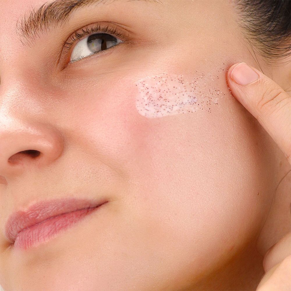 Gros plan sur un visage. Un gommage est appliqué sur la joue. La peau est visible.