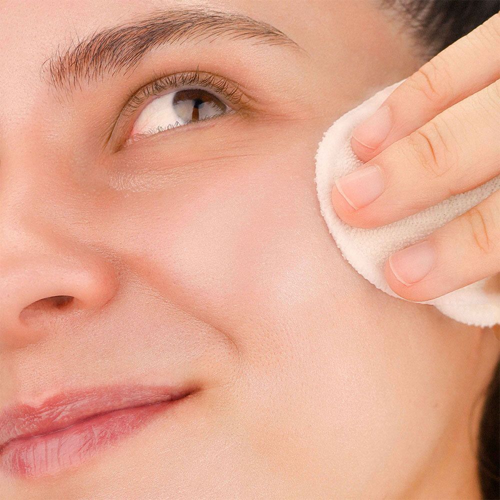 Gros plan d'un visage nettoyé avec un coton. La peau est visible.