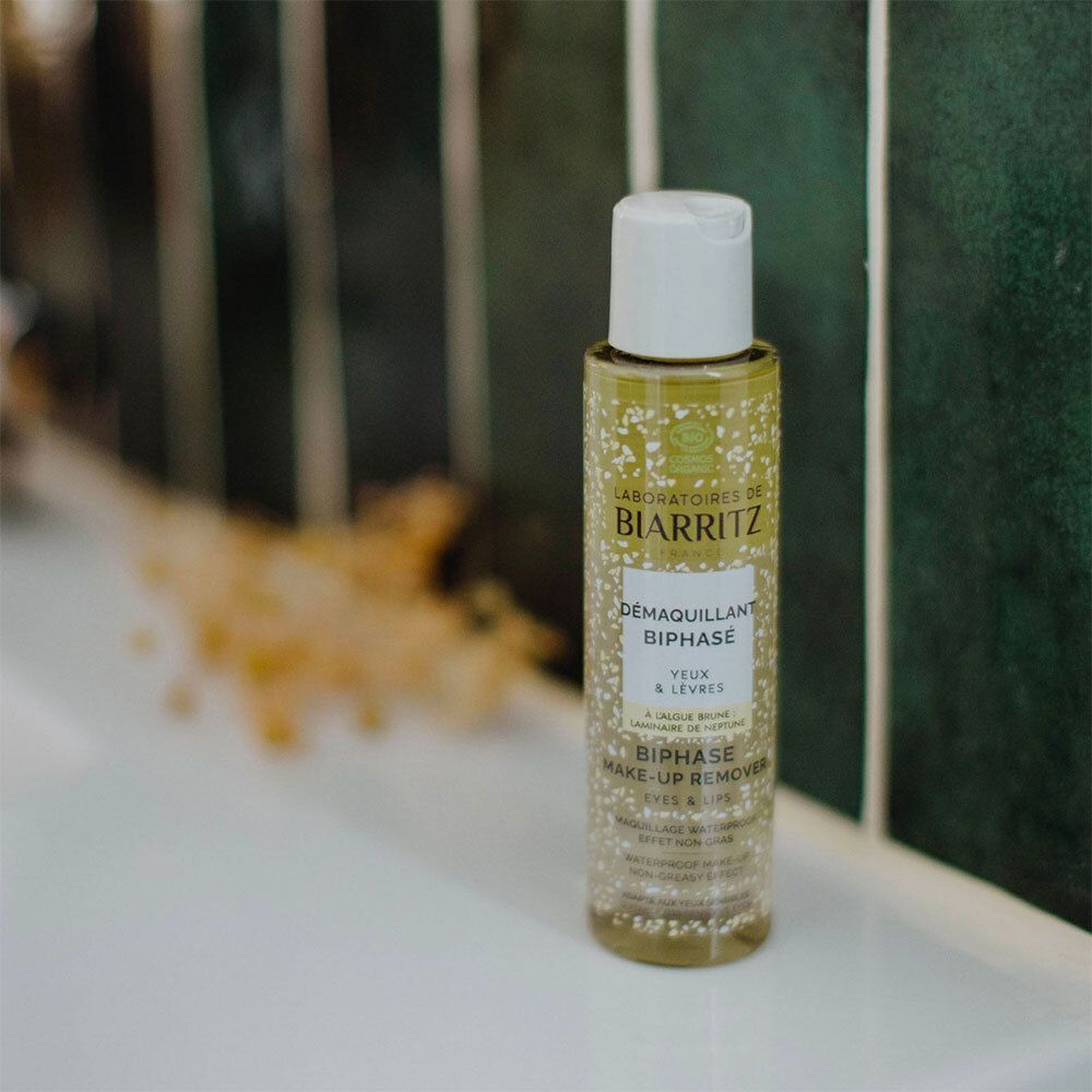 Flacon de Démaquillant Biphasé Yeux & Lèvres Bio sur une surface blanche. Fond vert.