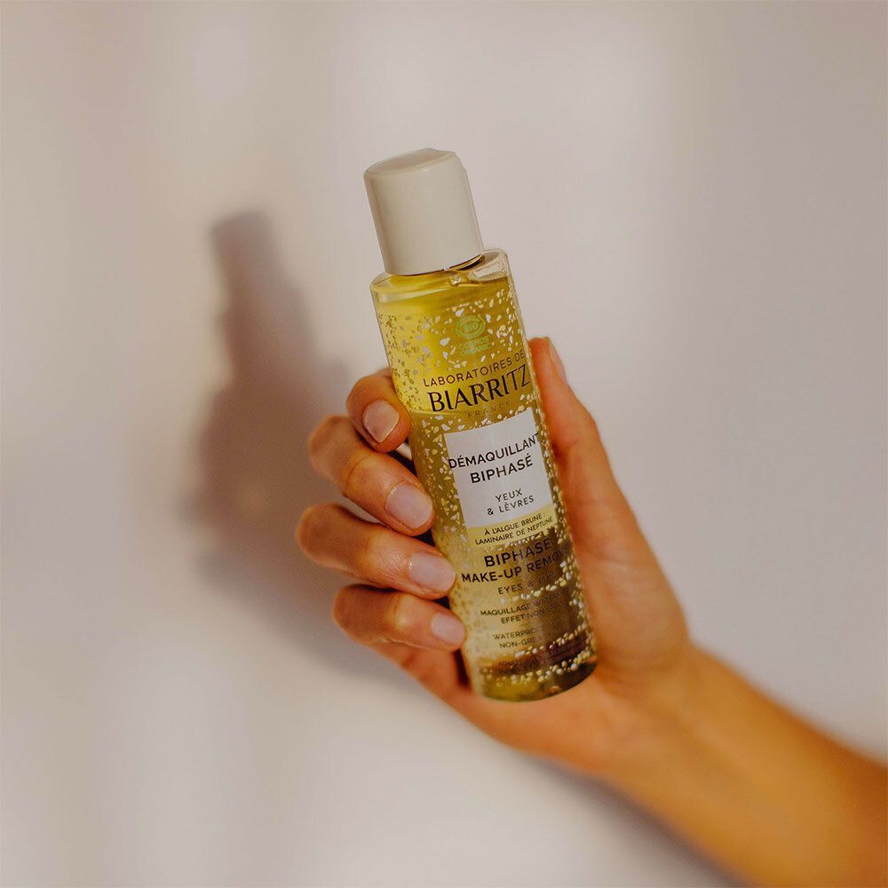 Une main tient un flacon de Démaquillant Biphasé Yeux & Lèvres Bio. Le fond est blanc.