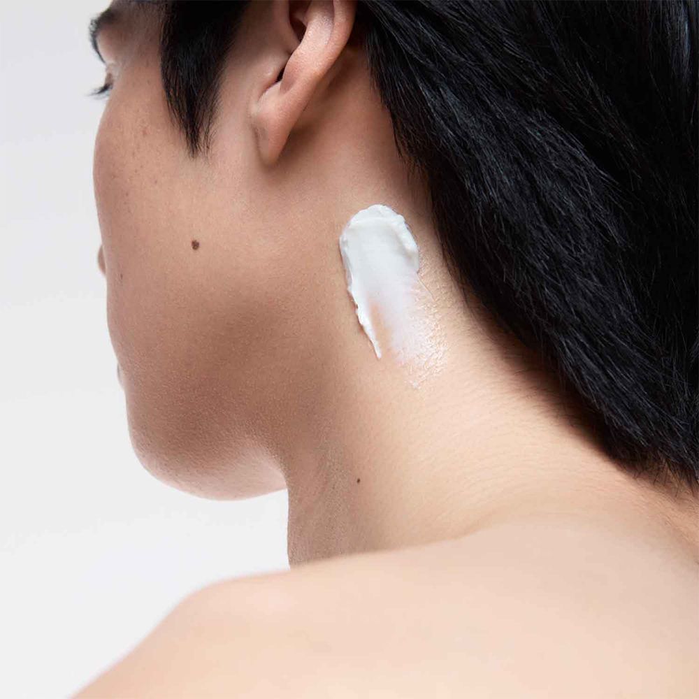 Personne avec de la crème sur le cou. La crème est blanche. Fond clair.