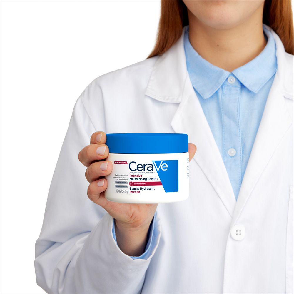 Personne tenant un pot blanc à couvercle bleu. Inscription CeraVe, Intensive Moisturising Cream, Baume Hydratant Intensif.