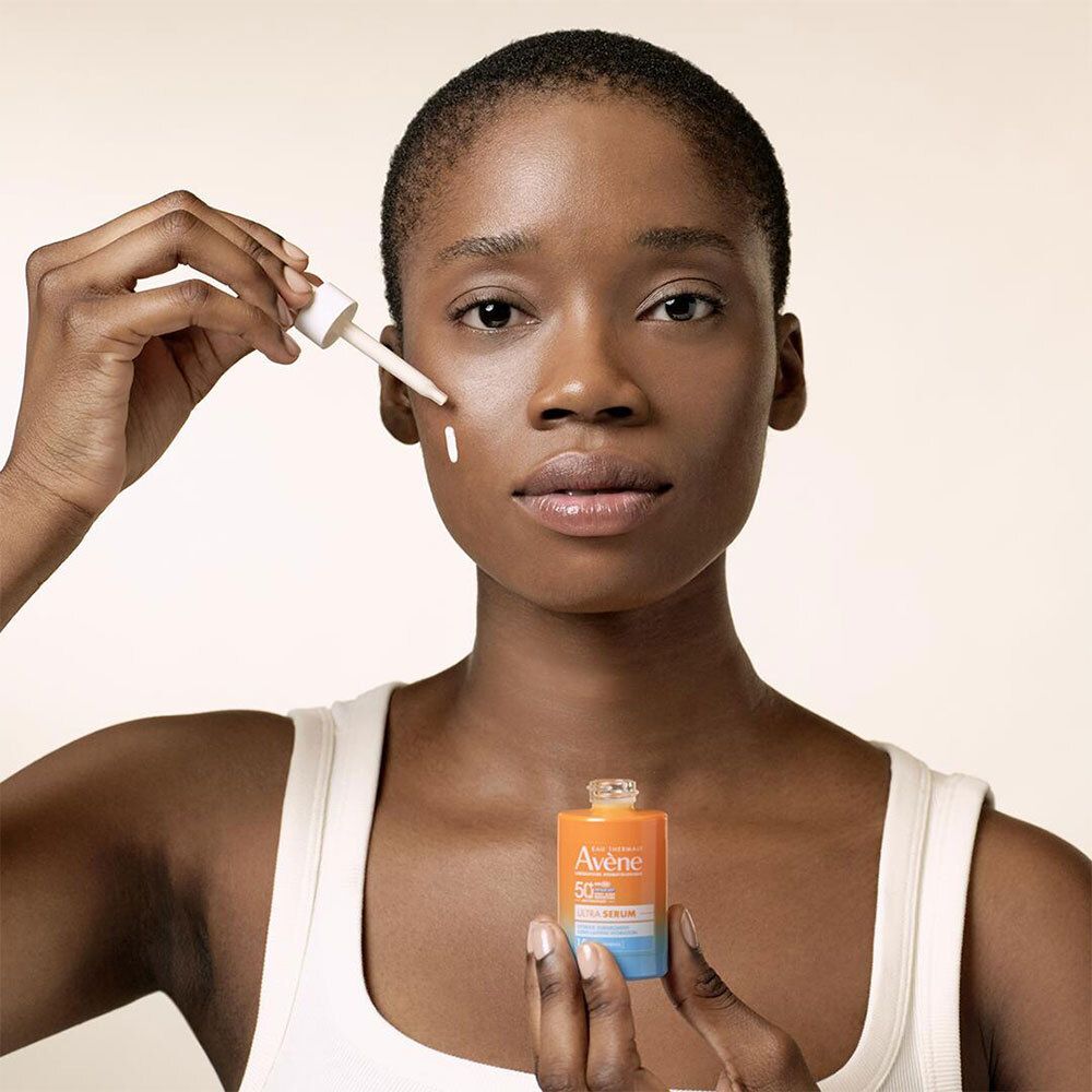 Femme tenant flacon et pipette de sérum. Porte un débardeur blanc. Le sérum est appliqué sur la peau.