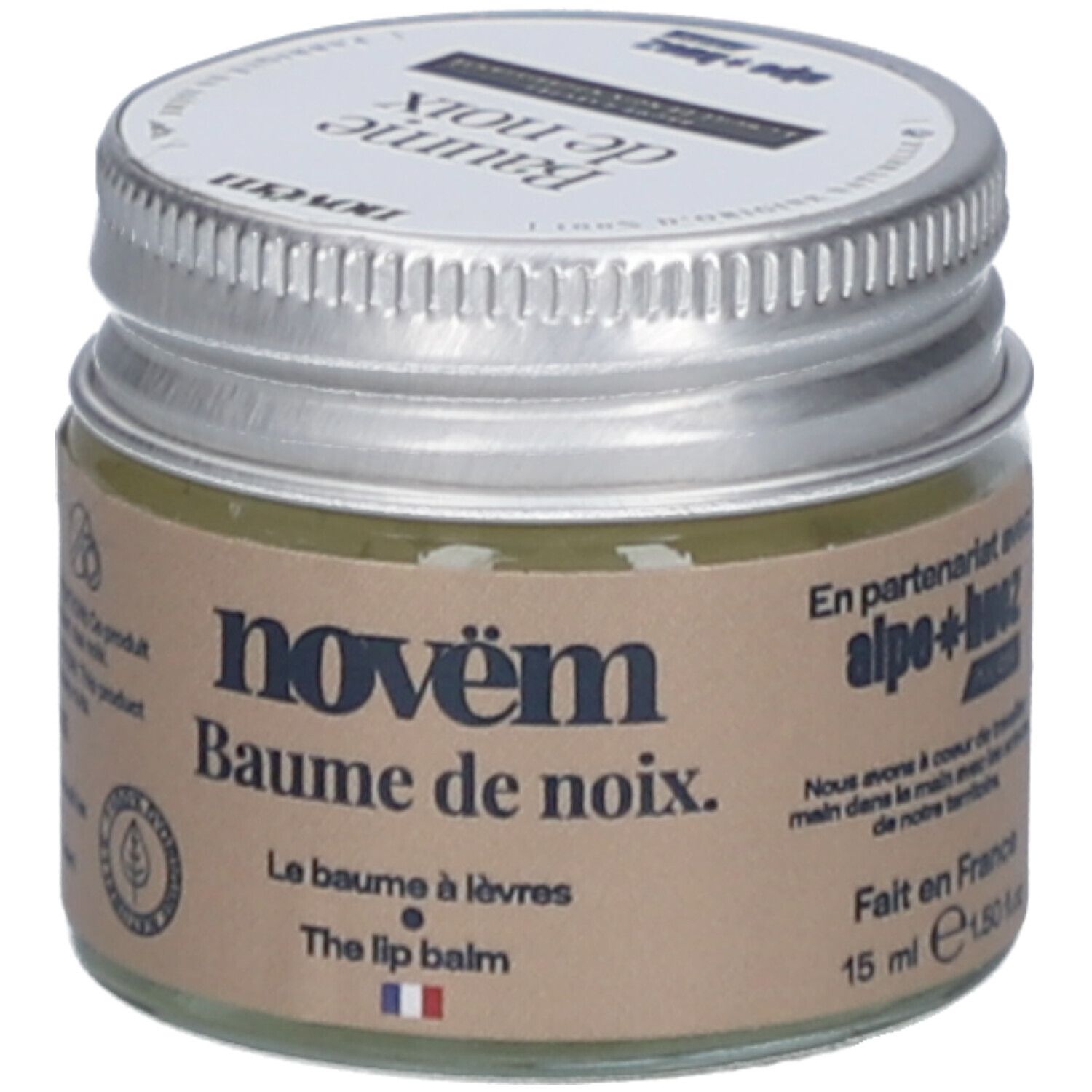 Pot en verre avec couvercle argenté. Étiquette avec nom du produit: novëm Baume de noix. Le Baume à lèvres. The lip balm. 15 ml. Fabriqué en France.
