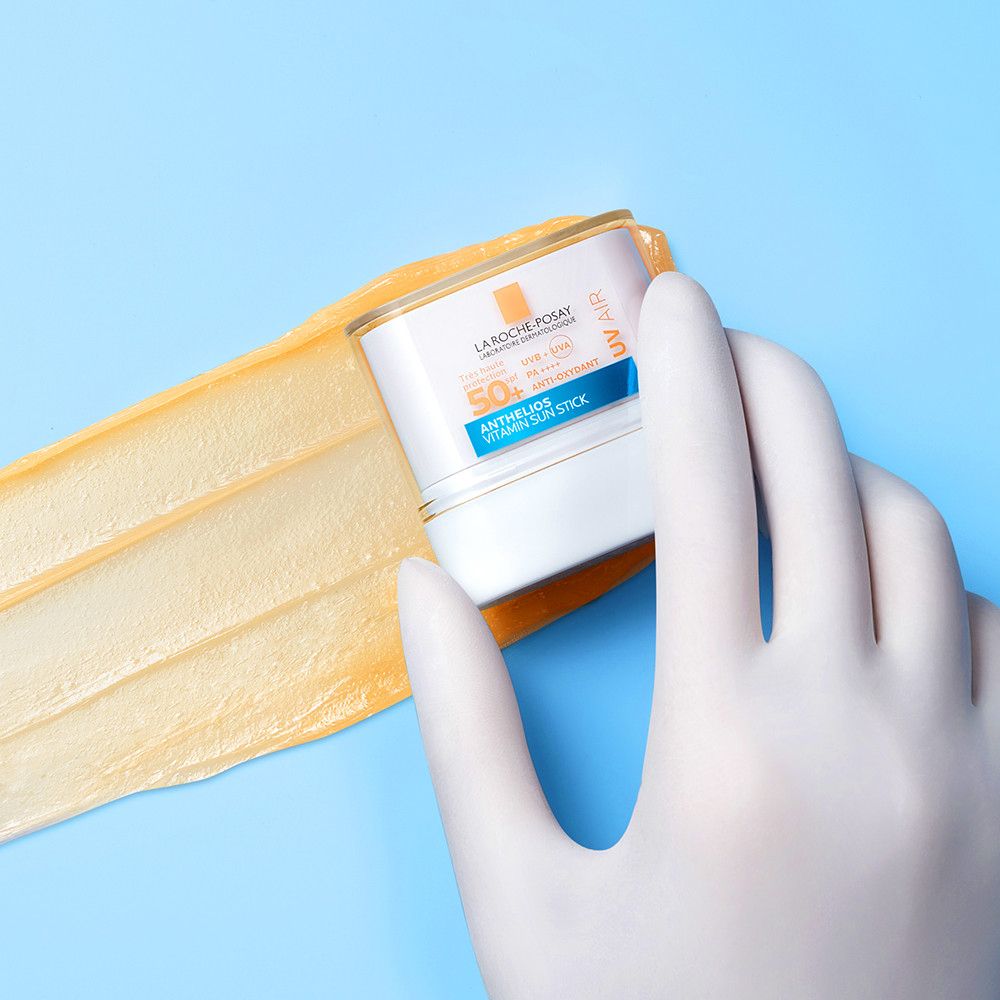 Main gantée tenant un stick blanc. Produit appliqué sur fond bleu.