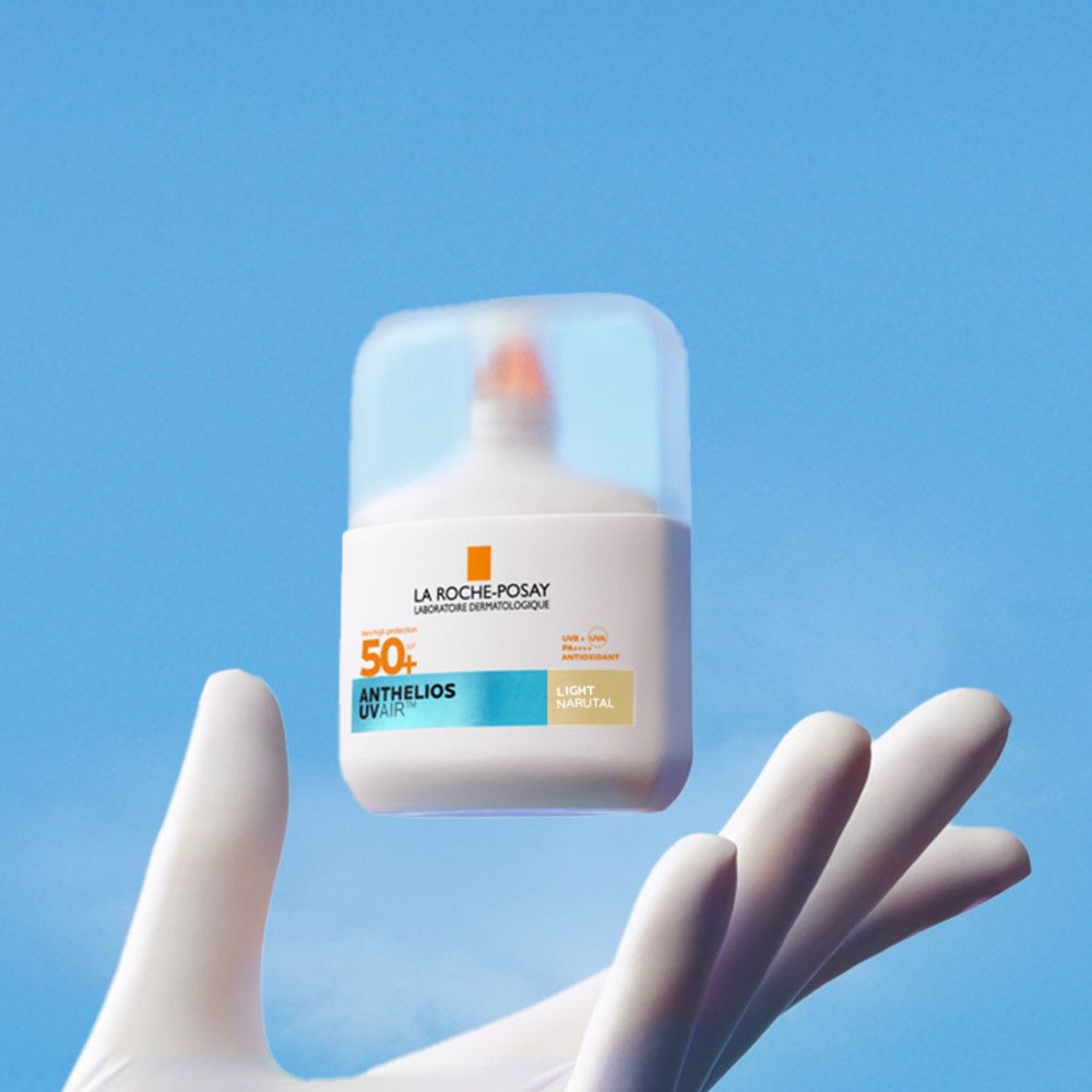 Flacon blanc avec bouchon rabattable, tenu dans une main. Inscription: Anthelios UVAir Serum Sunscreen SPF50+.