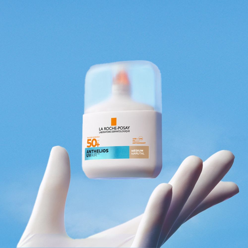 Flacon blanc avec couvercle transparent tenu par une main gantée. Inscriptions: Anthelios UVAir Serum Sunscreen SPF50+.