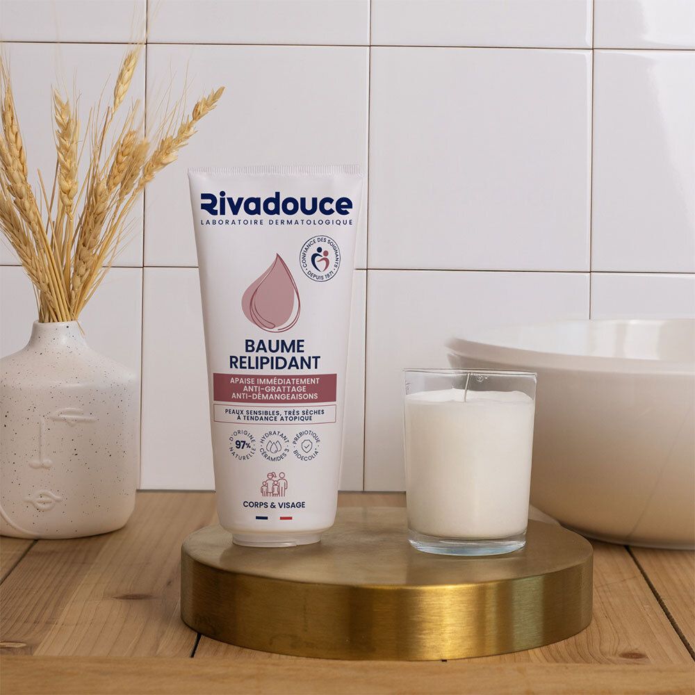 Produit sur surface dorée. Tube blanc Rivadouce. Bougie et vase avec épis de blé en arrière-plan. Mur carrelé.