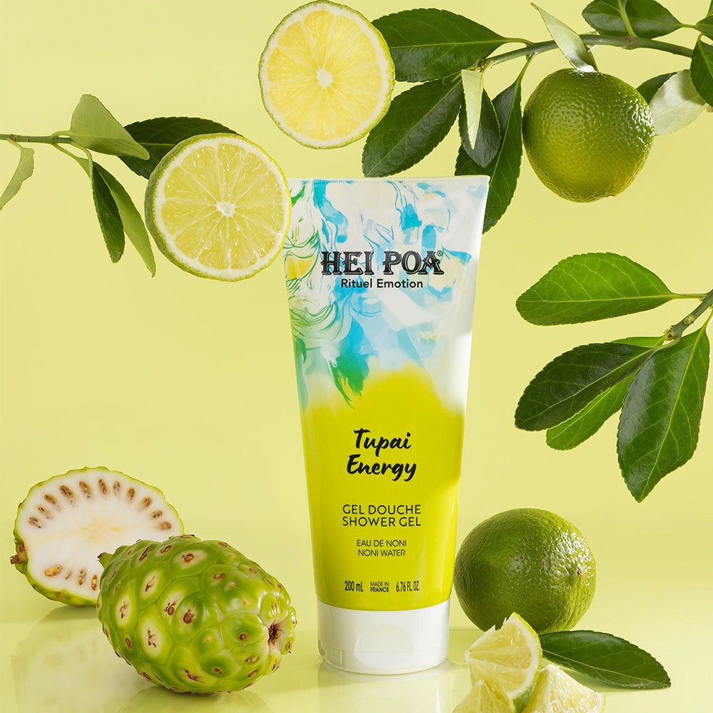 Tube de gel douche Hei Poa Tupai Energy entouré de fruits de noni et de citrons verts.