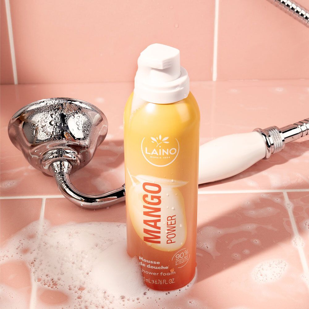 Mousse de douche LAINO Mango Power à côté d'un pommeau de douche dans une cabine.