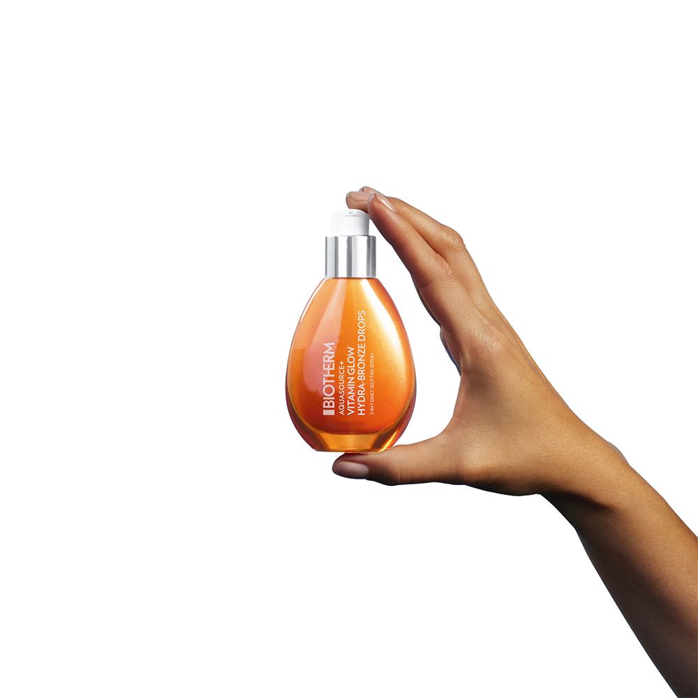 Main tenant un flacon orange avec pompe, sérum Biotherm Aquasource+ Vitamin Glow Hydra-Bronze Drops.