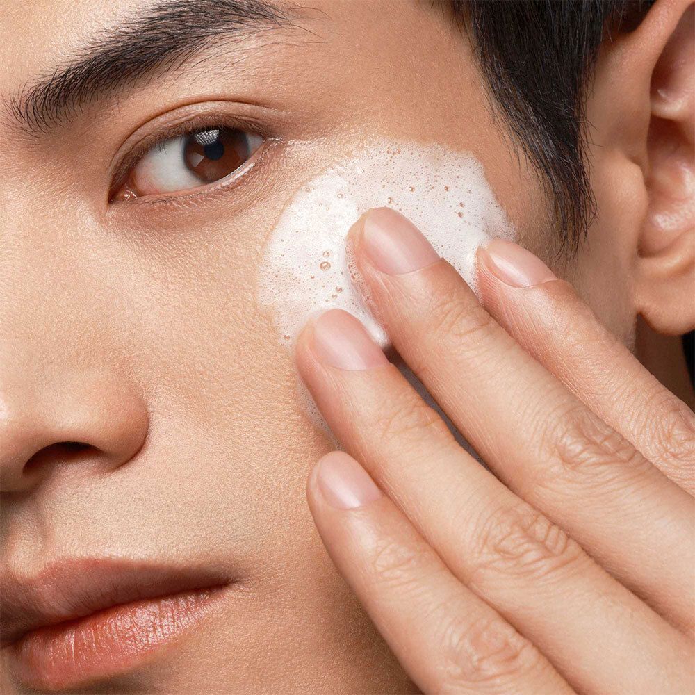 Gros plan d'un homme appliquant un produit moussant sur son visage. Peau claire, cheveux foncés.