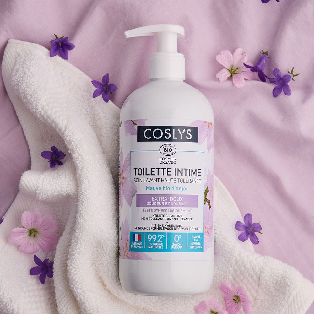 Flacon blanc avec pompe. Étiquette : Coslys, Toilette Intime, Extra-Doux. Sur serviette blanche, décoré de fleurs.