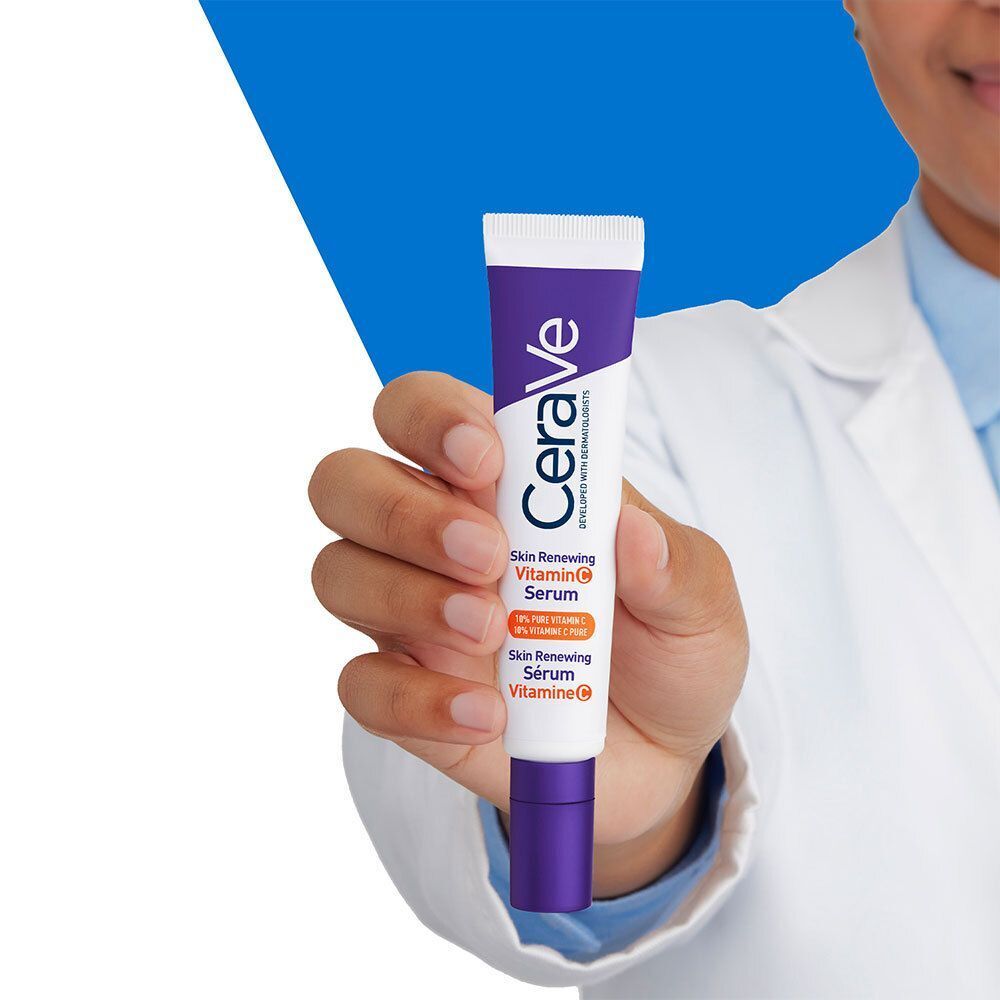 Une personne tient un tube de sérum CeraVe Skin Renewing Vitamin C. Blouse blanche en arrière-plan.