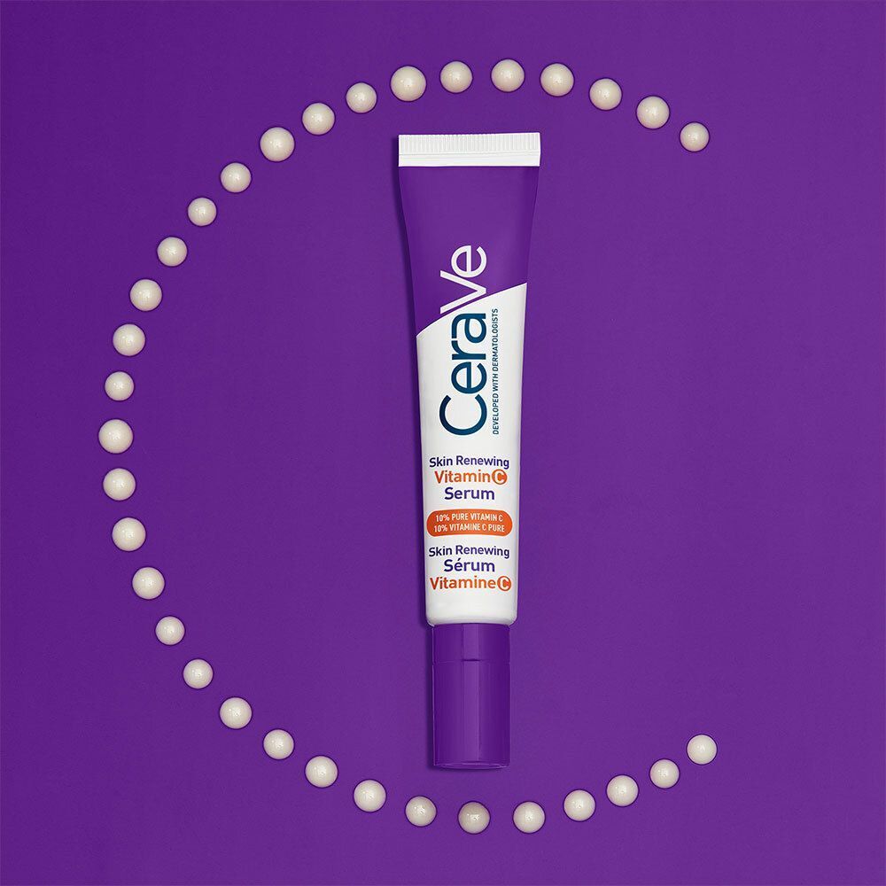 Tube de sérum CeraVe Skin Renewing Vitamin C entouré de perles blanches. Fond violet.