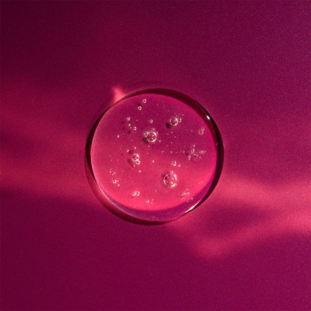 Goutte de liquide rose, ronde, avec bulles. Fond rose.