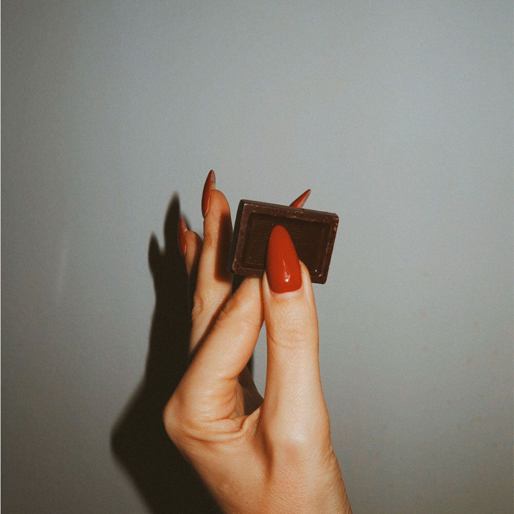 Main avec vernis rouge tenant un carré de chocolat noir.