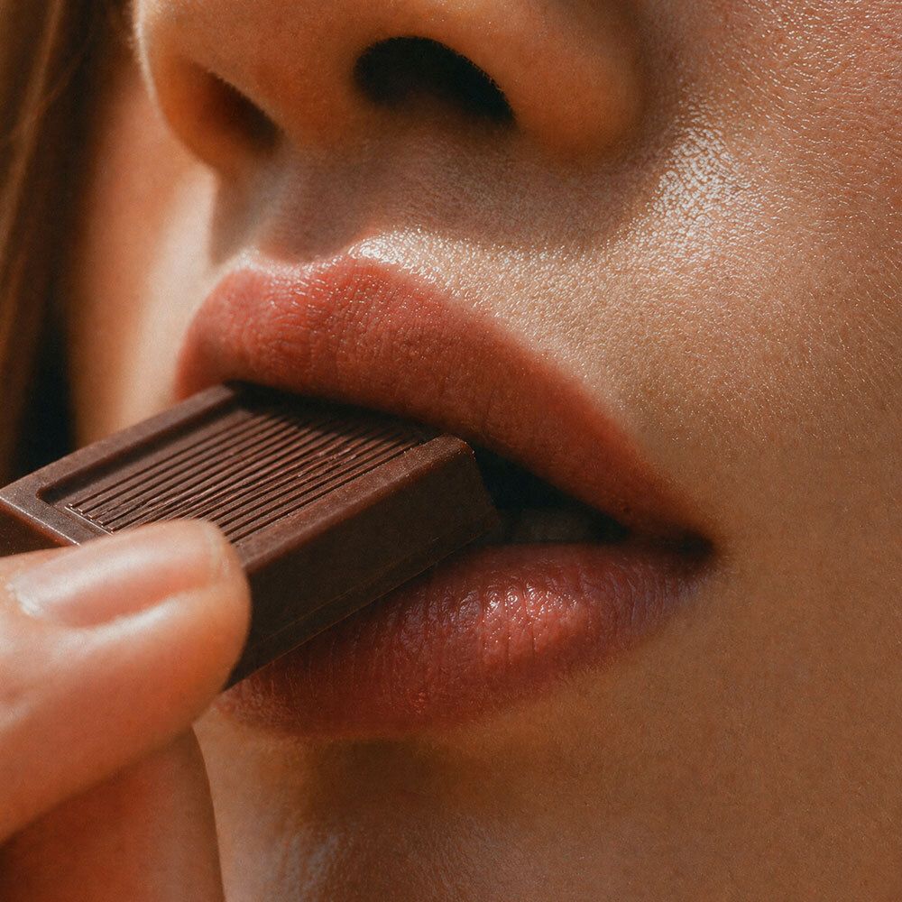 Gros plan sur des lèvres mangeant un carré de chocolat noir.