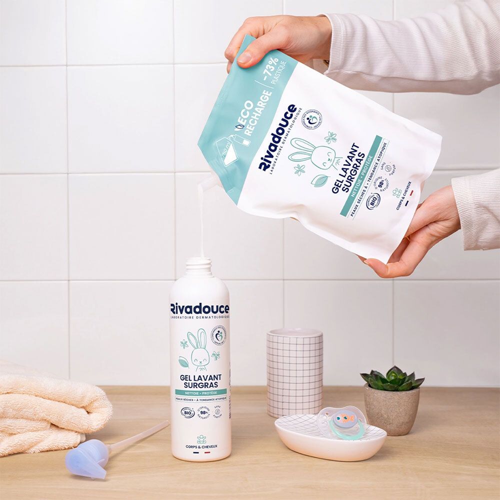 Mains versant le contenu d'un sachet dans un flacon. Flacon et sachet avec logo, texte "GEL LAVANT SURGRAS". Autres objets: serviette, porte-savon.