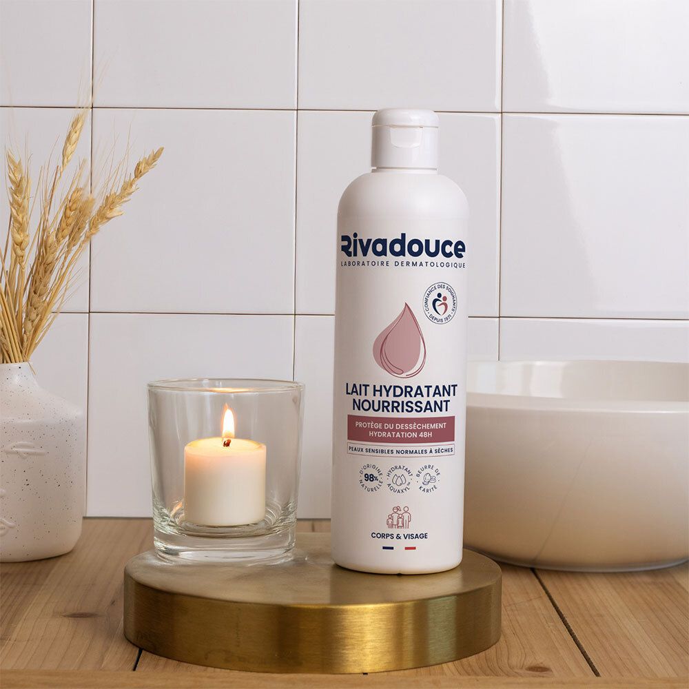Flacon blanc avec étiquette rose. Inscription: Rivadouce, Lait Hydratant Nourrissant. Sur un socle avec bougie et décoration.