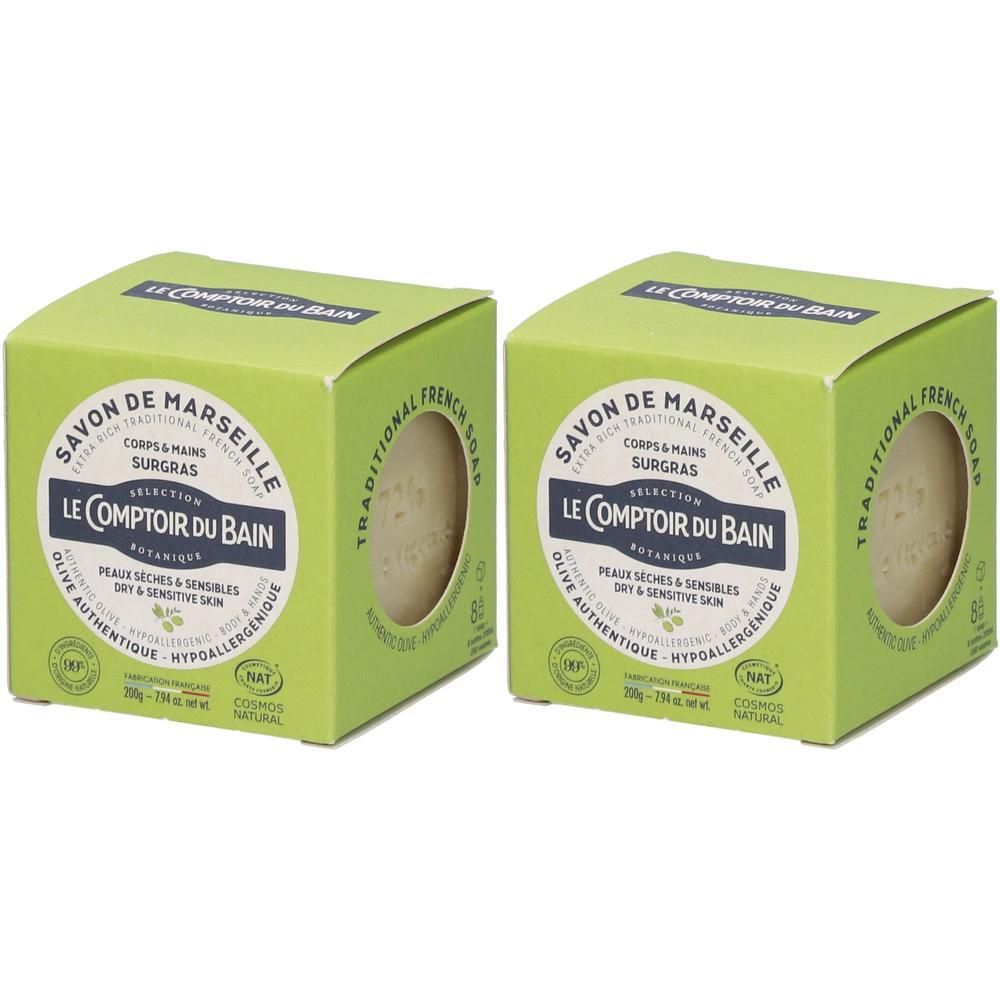 Deux boîtes vertes de savon. Inscription: SAVON DE MARSEILLE, LE COMPTOIR DU BAIN. Savon visible à travers une fenêtre.