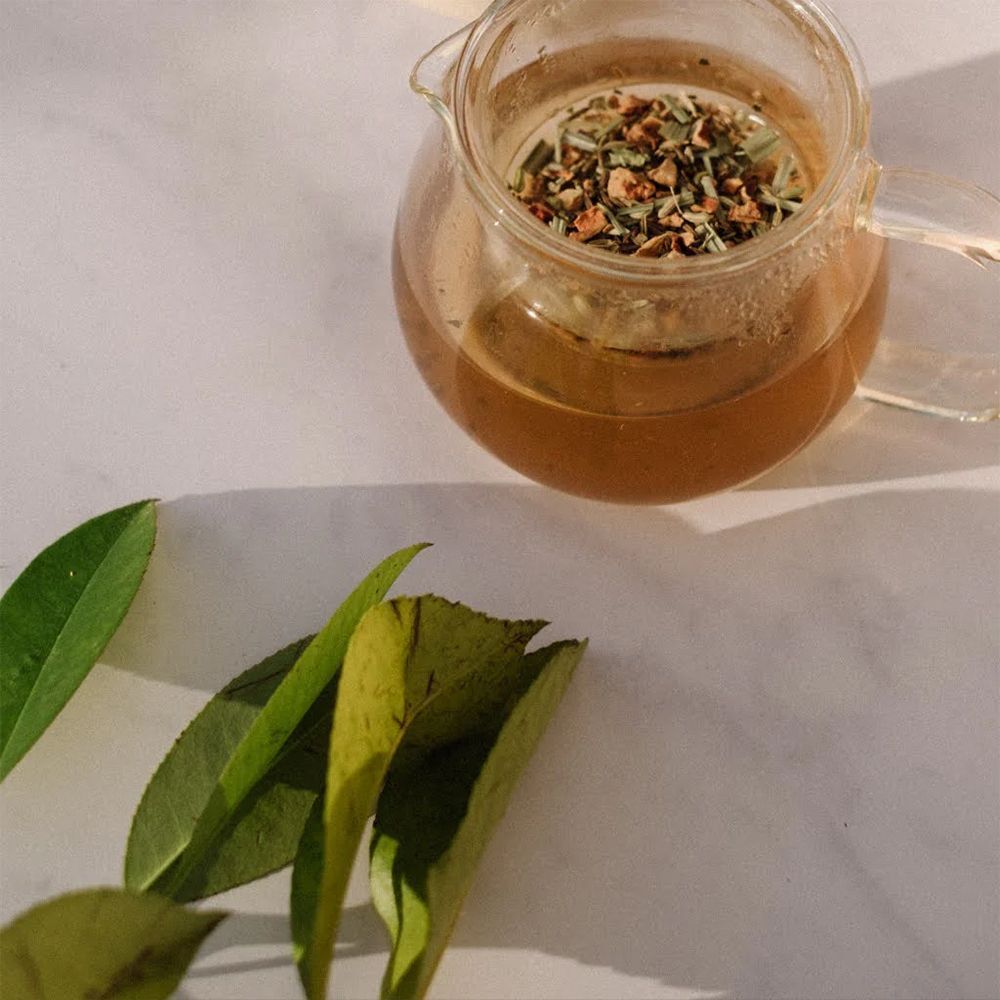 Pichet en verre avec boisson et herbes. Feuilles vertes à côté.