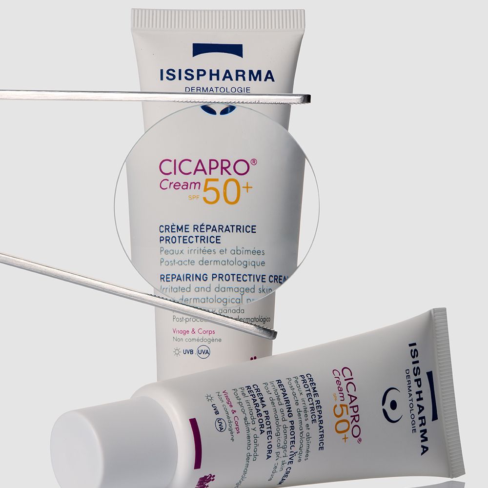Tube Isispharma Cicapro Cream SPF50+ en focus, avec une loupe et un autre tube en arrière-plan.