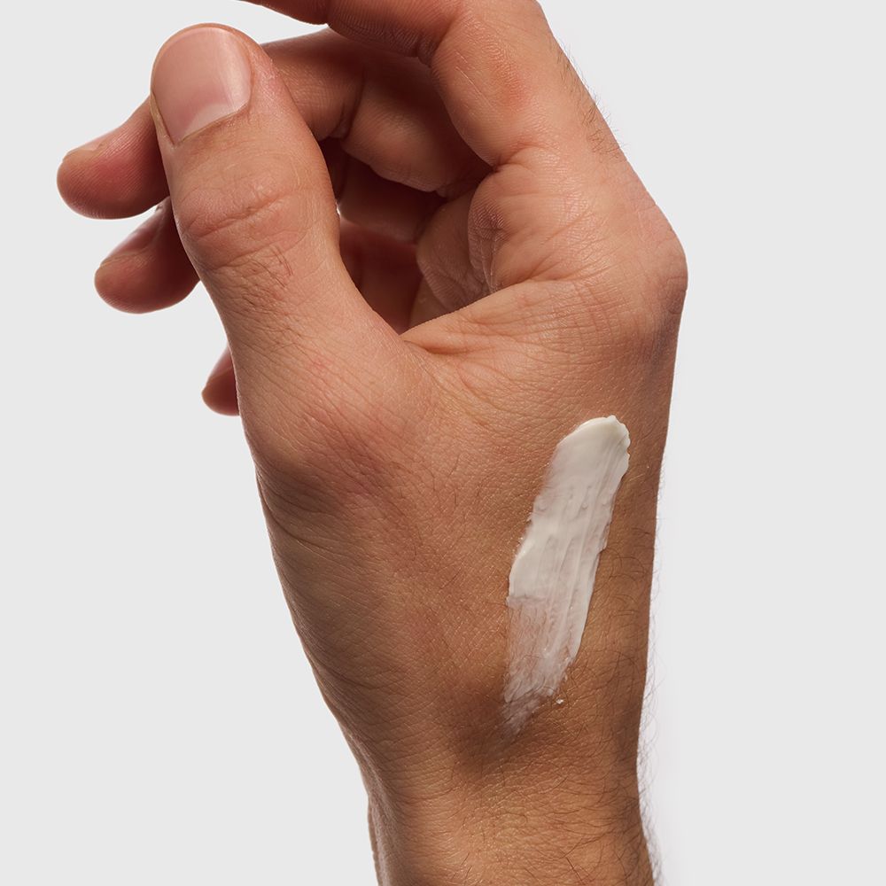 Main avec crème. Crème blanche sur la peau. Couleur de peau claire. Fond neutre.