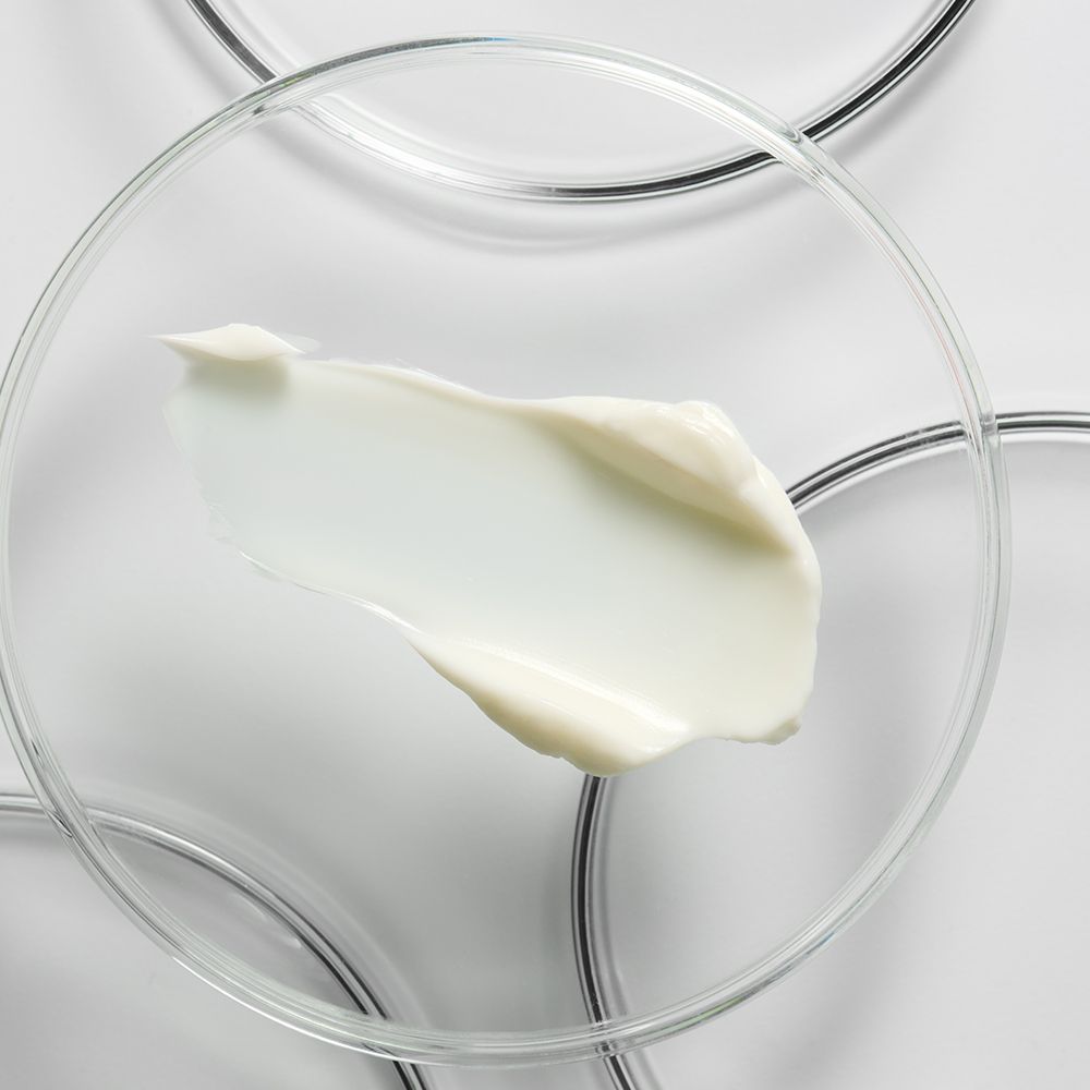 Goutte de crème blanche sur plaque de verre. Fond blanc. Plusieurs anneaux de verre.