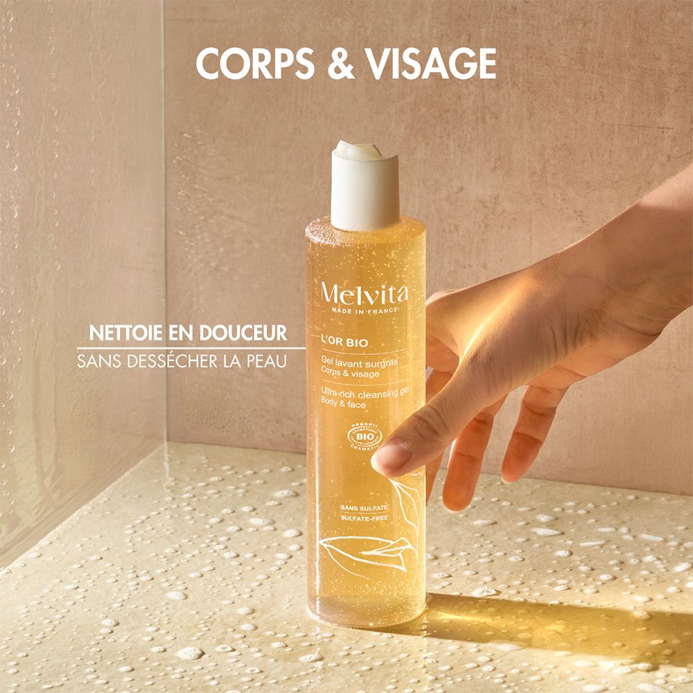 Gel douche Melvita en flacon, tenu par une main dans une douche. Texte : "CORPS & VISAGE".