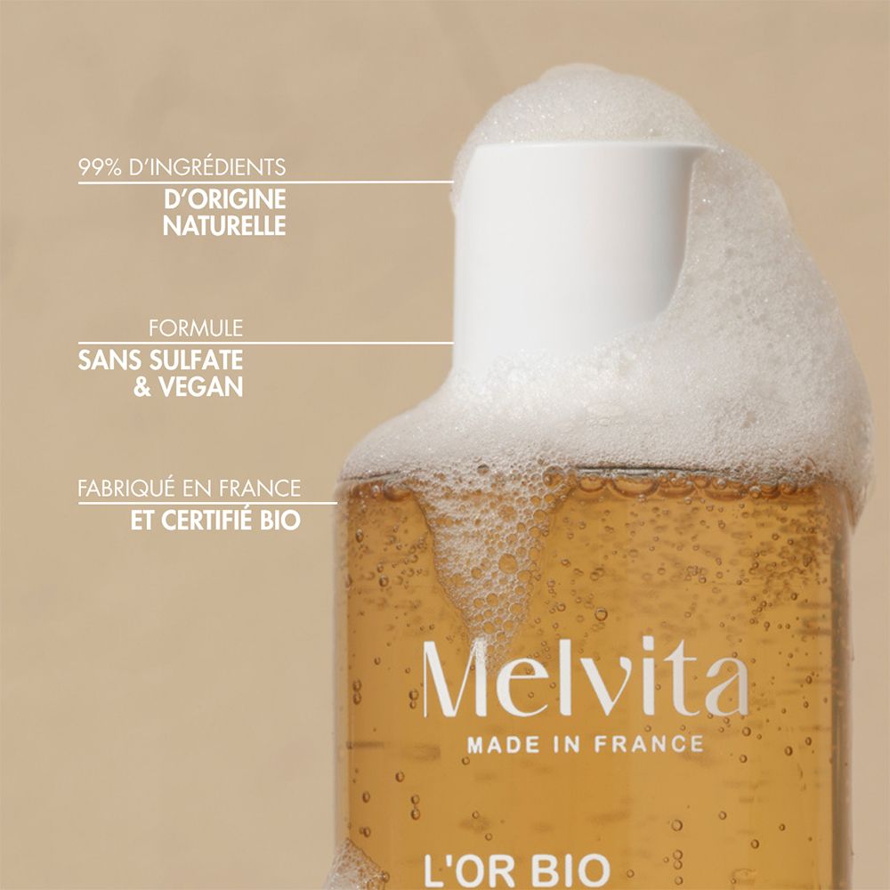 Gros plan du goulot d'un gel douche Melvita avec de la mousse. Texte : "99% D'INGRÉDIENTS D'ORIGINE NATURELLE", "FORMULE SANS SULFATE & VEGAN", "FABRIQUÉ EN FRANCE ET CERTIFIÉ BIO".